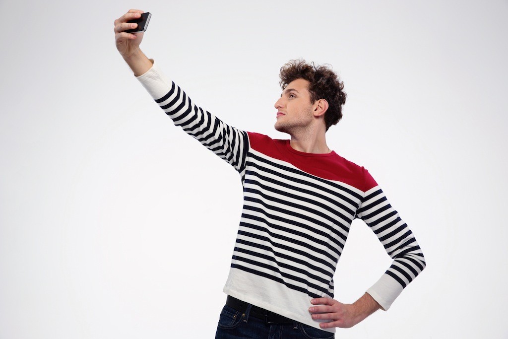 Side View Portrait Of A Man Making Selfie Photo Over Gray Background